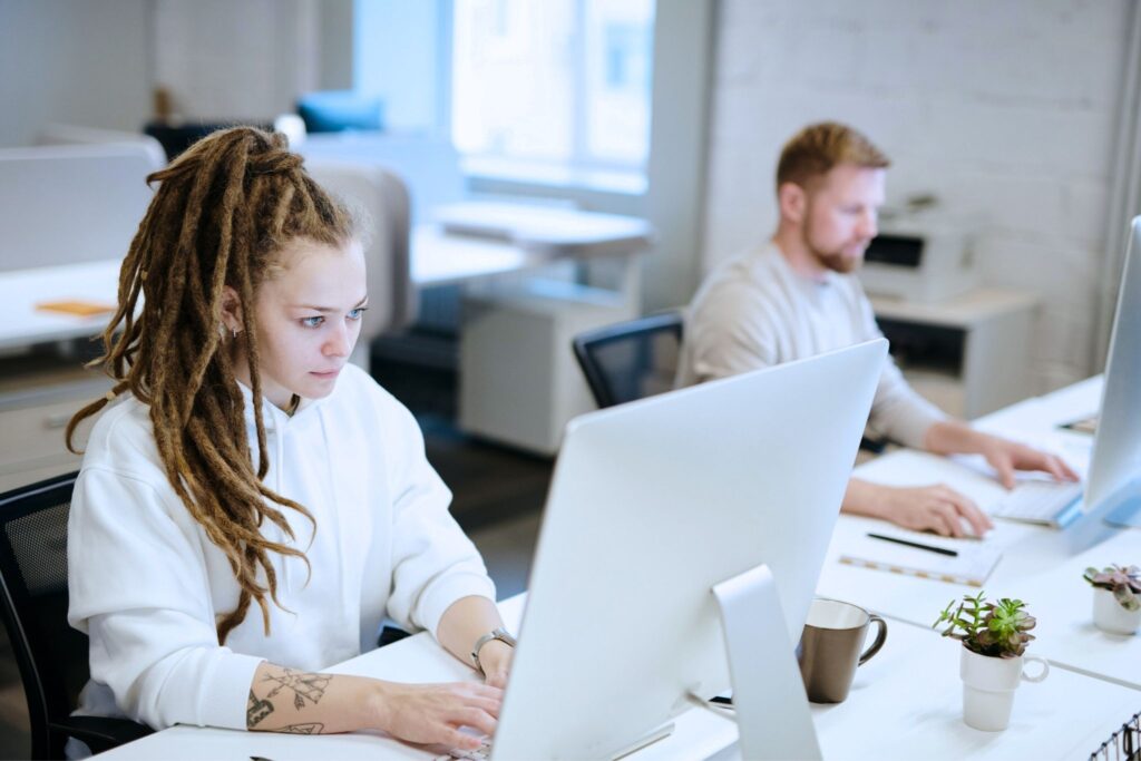 Two people working on the computers at the office.