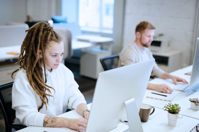 Two people working on the computers at the office.